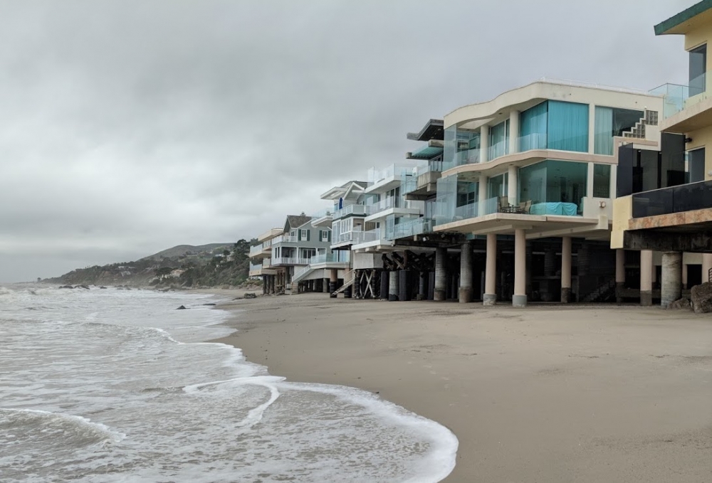 The wash recedes on a sandy beach mere meters from multi-million-dollar beach houses perched upon struts and stilts.